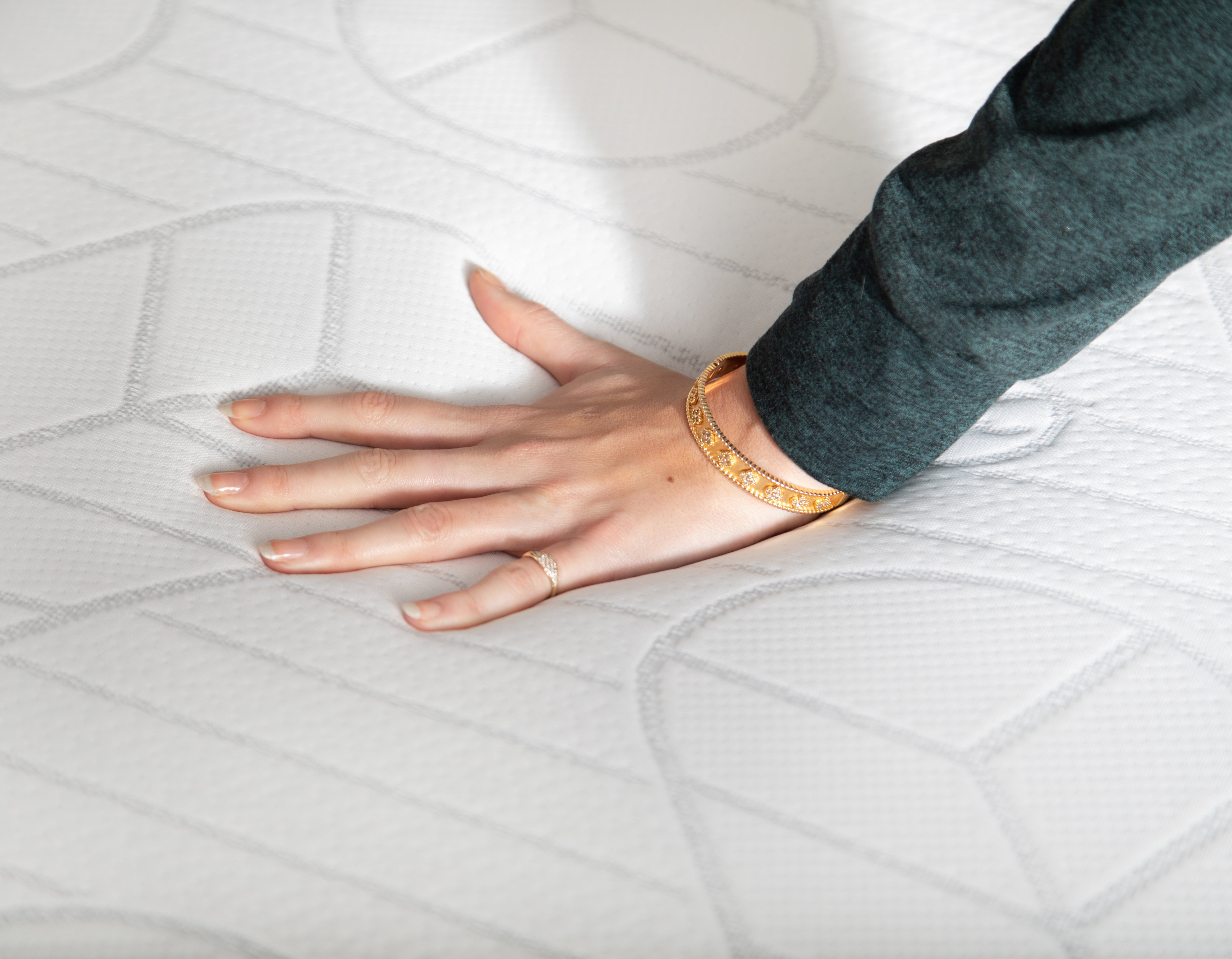 Hand wearing a gold bracelet on a textured white mattress topper by Sleepyhead